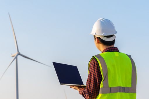 Man with laptop looking at windmill